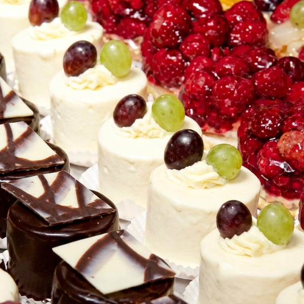 Rows of assorted mini pastries, including chocolate cakes, fruit tarts, and cream cakes with grapes and raspberries.