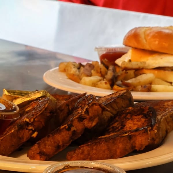 Plate of grilled meat skewers with dipping sauce, alongside a cheeseburger and fries on a restaurant table.
