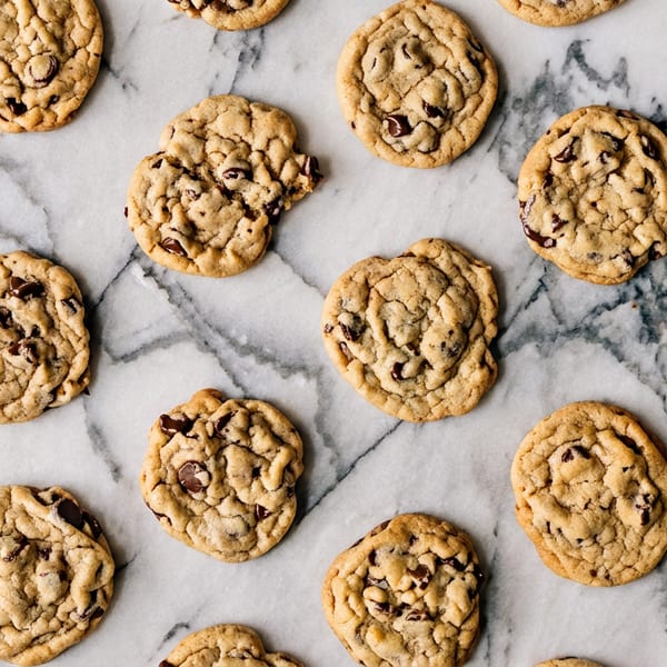 Many chocolate chip cookies scattered across a white and gray marble surface.