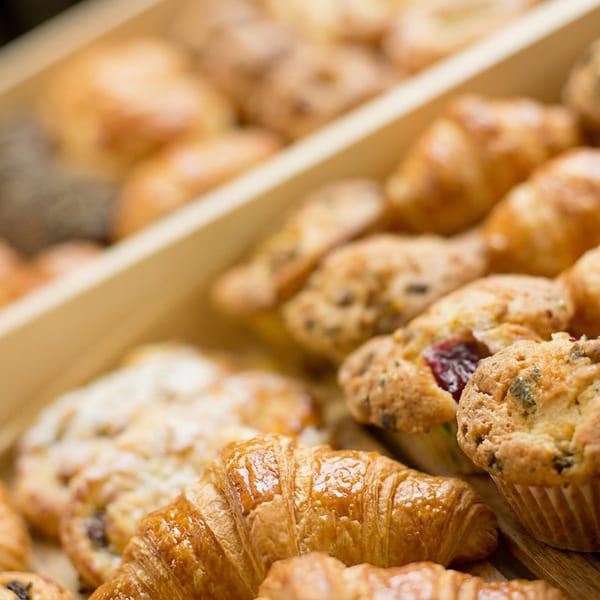 Assortment of golden croissants and various muffins in wooden trays, ready for breakfast.