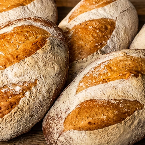 Several loaves of freshly baked, rustic sourdough bread with flour dusting on a wooden surface.